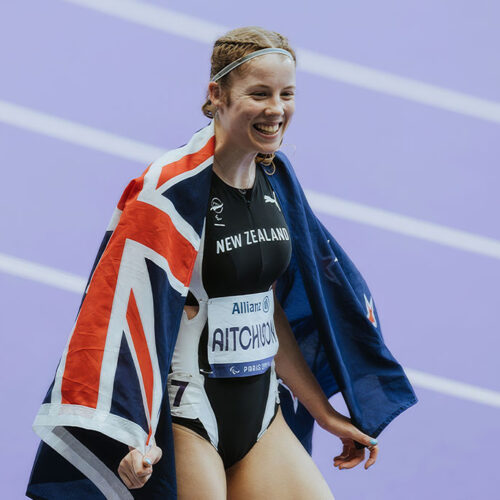Danielle Aitchison on a running track with a NZ flag over her shoulders