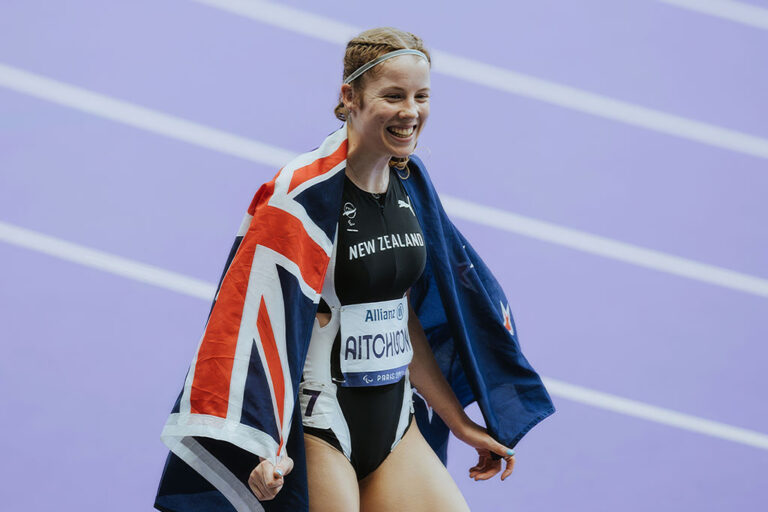 Danielle Aitchison on a running track with a NZ flag over her shoulders
